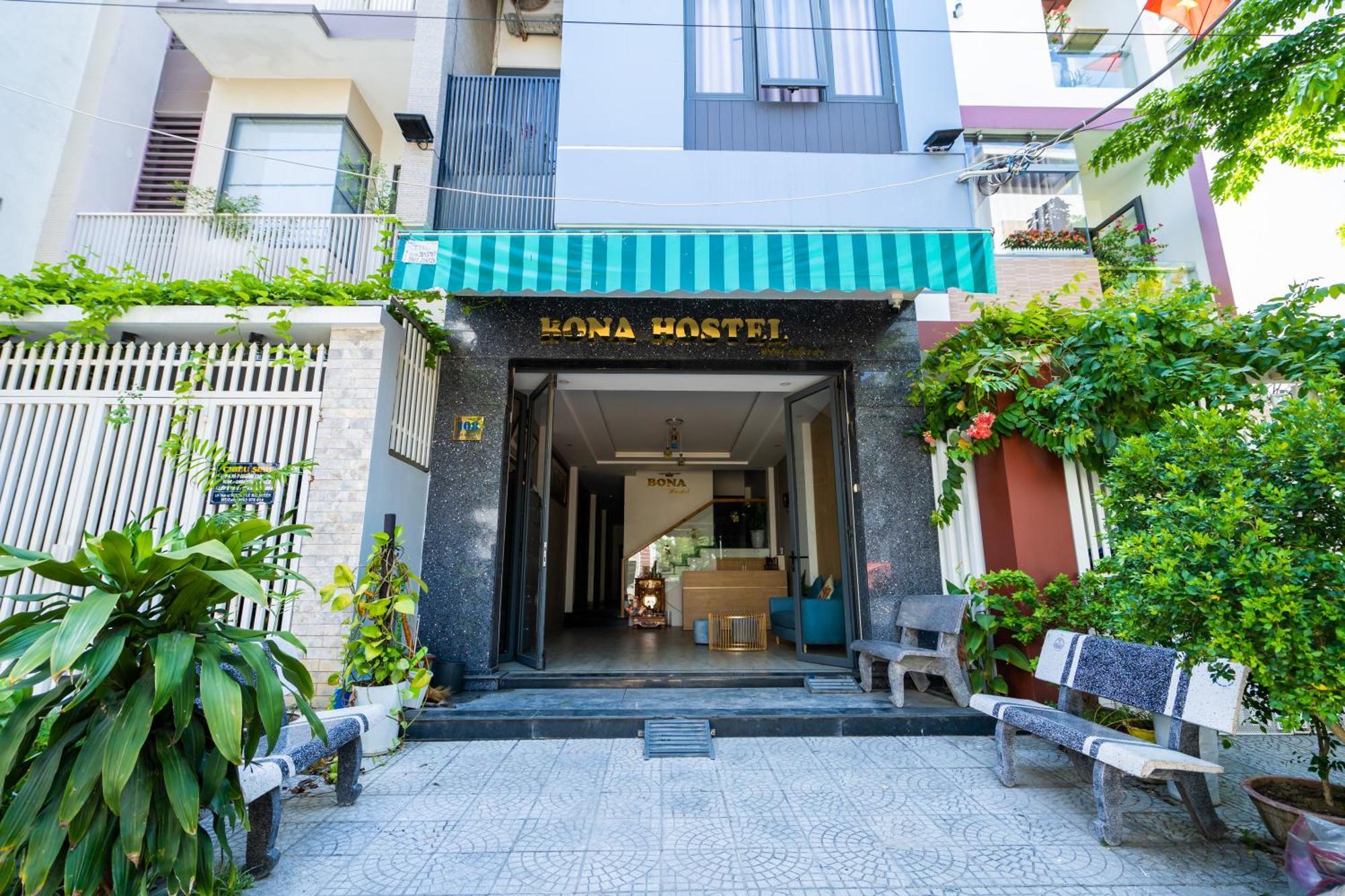 Mặt tiền Bona Hostel với mái che sọc xanh, cửa mở rộng và nhiều cây xanh hai bên