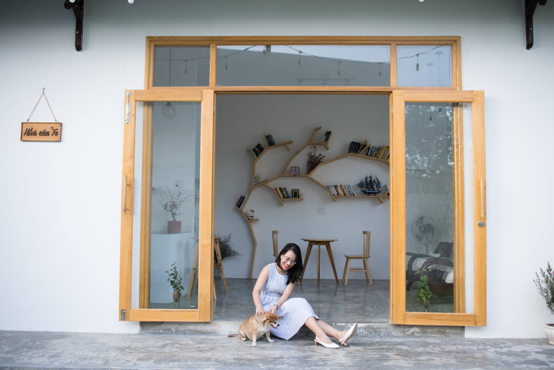 Phụ nữ ngồi trước cửa gỗ mở, vuốt ve chó bên biển hiệu Nhà của Te