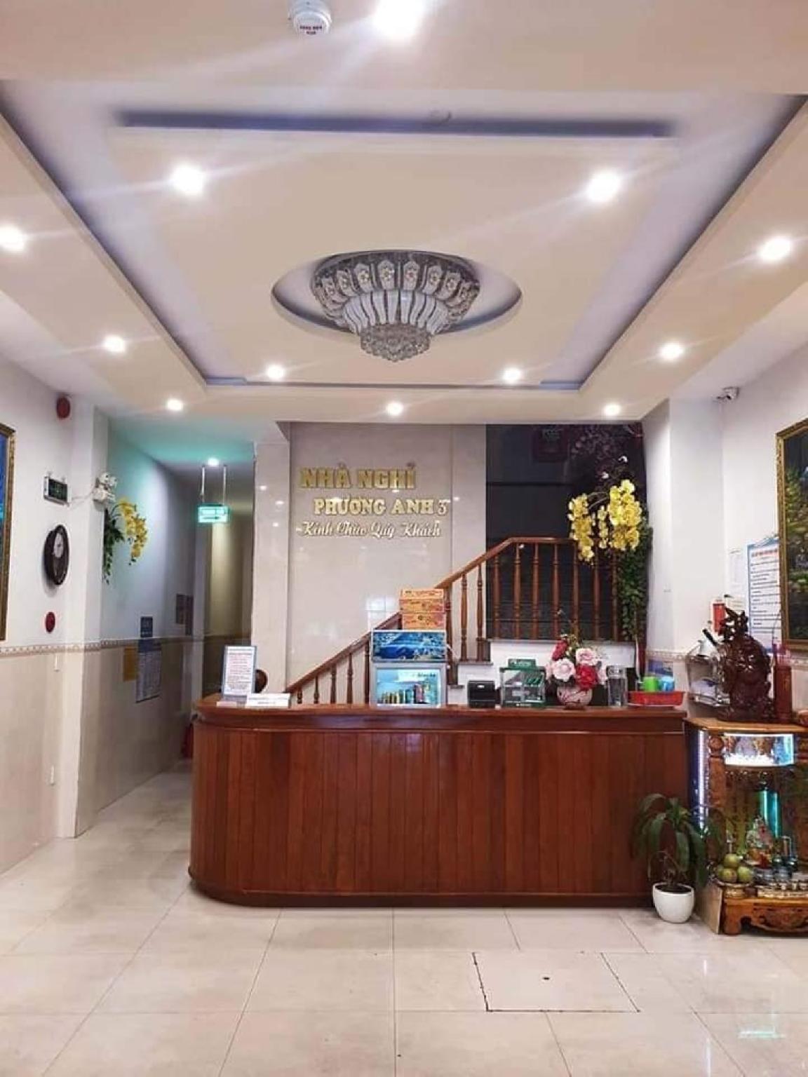 Quầy lễ tân bằng gỗ dưới đèn chùm, phía sau có biển Nhà nghỉ Phương Anh 3 và cầu thang