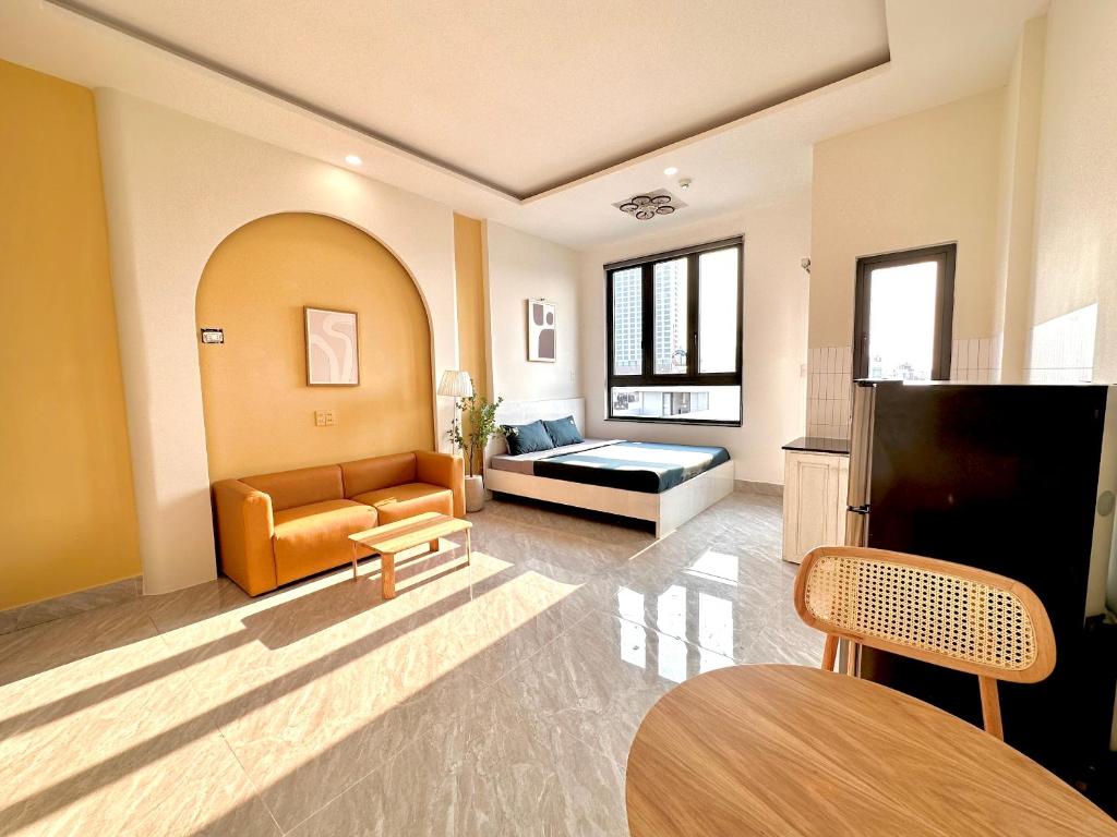 Phòng studio sáng màu với giường đôi, sofa cam, bàn ăn gỗ và tủ lạnh cạnh bếp nhỏ