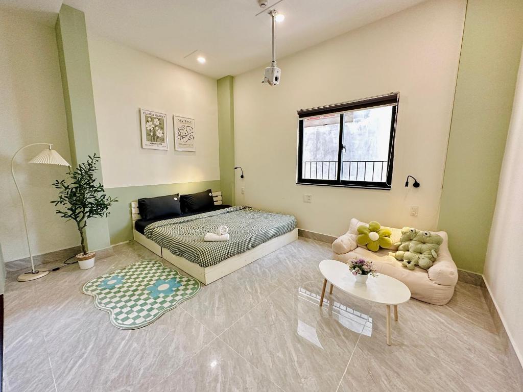 Phòng ngủ tông xanh kem với giường đôi, sofa thấp đặt thú bông, bàn trà trắng và máy chiếu treo trần