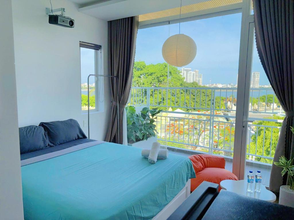 Phòng ngủ với ga xanh ngọc, máy chiếu treo trần và cửa kính lớn nhìn ra sông cùng thành phố
