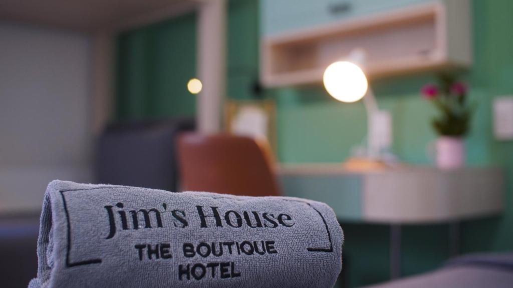 Khăn xám cuộn thêu tên Jim's House đặt trước bàn làm việc có đèn tròn và chậu hoa