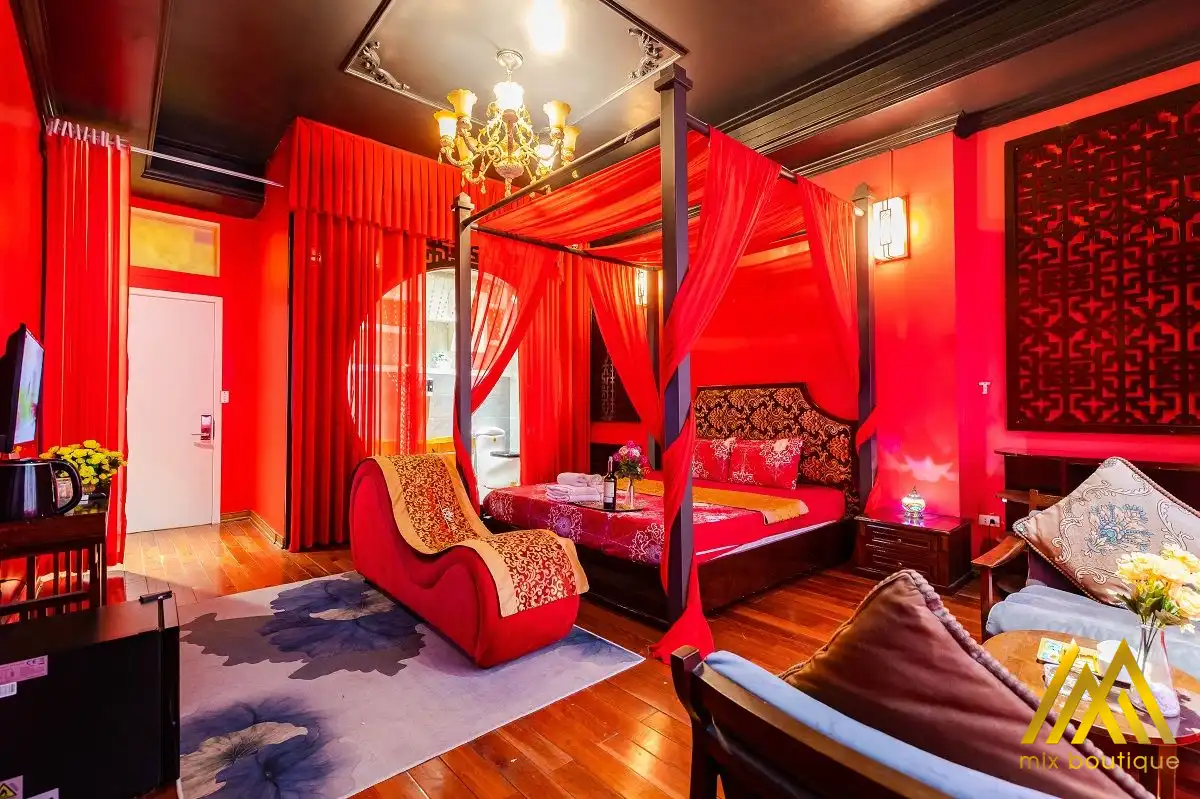 Phòng ngủ tông đỏ với giường bốn cọc phủ rèm, ghế bành, sofa và đèn chùm kiểu cổ điển