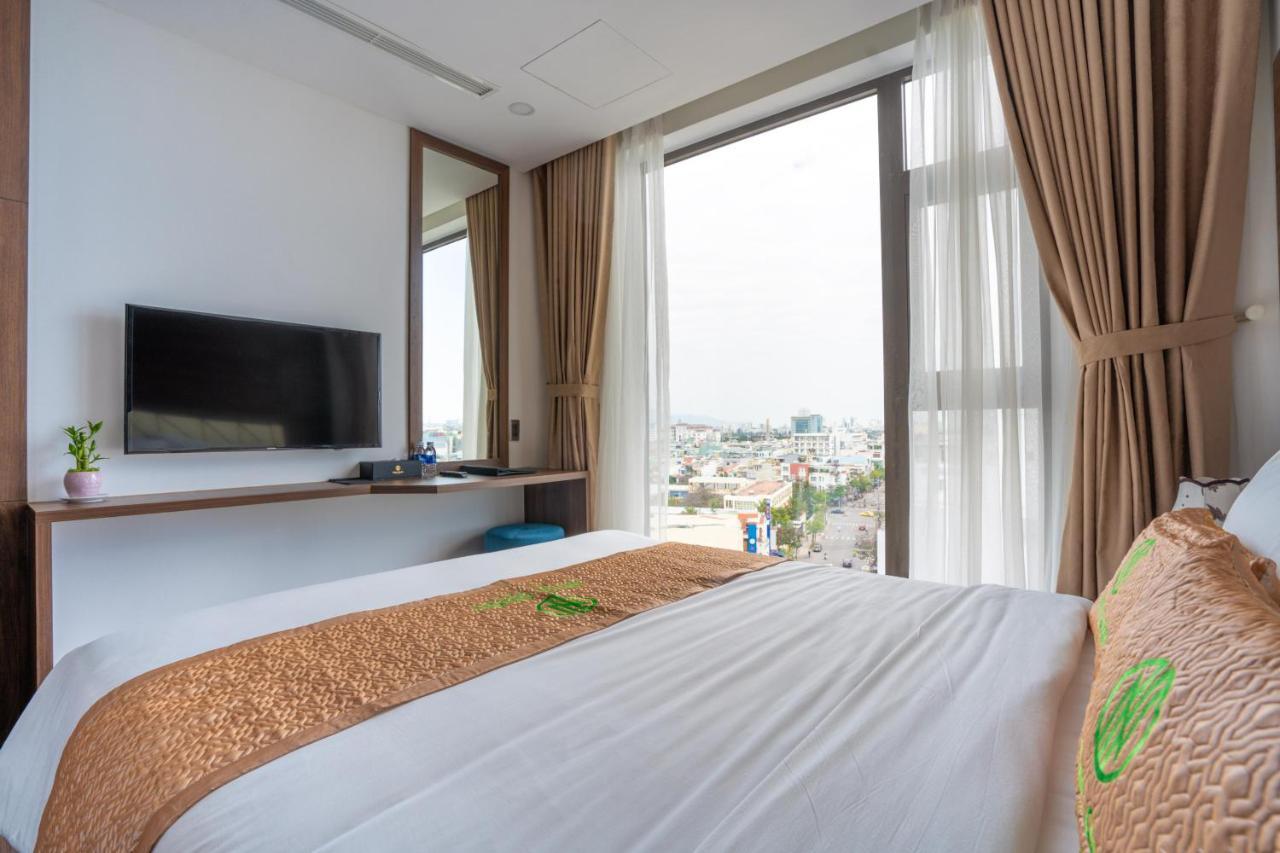 Phòng ngủ đôi với ga trắng, rèm nâu, tivi treo tường và cửa kính lớn nhìn ra thành phố