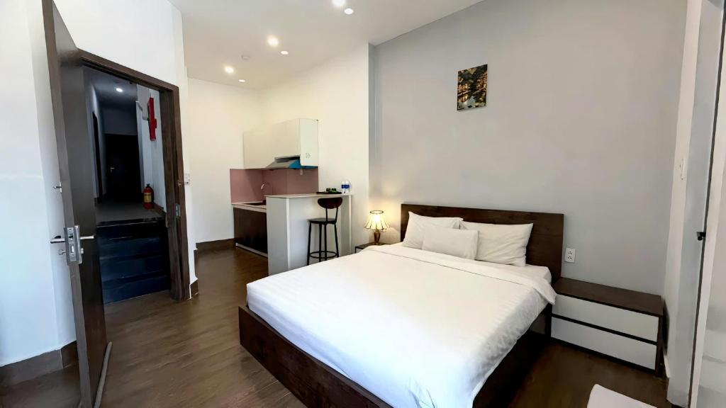 Phòng ngủ có giường đôi ga trắng, đầu giường gỗ, tủ đầu giường và quầy bếp nhỏ phía sau