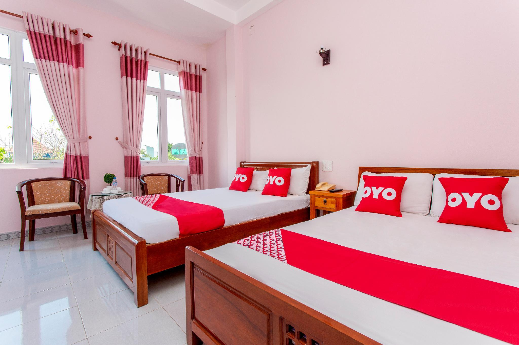 Phòng ngủ hai giường gỗ với chăn phủ đỏ, gối OYO và bàn trà cạnh cửa sổ