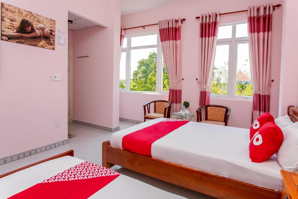 Phòng ngủ hai giường gỗ, tường hồng, rèm sọc đỏ trắng và cửa sổ nhìn ra cây xanh