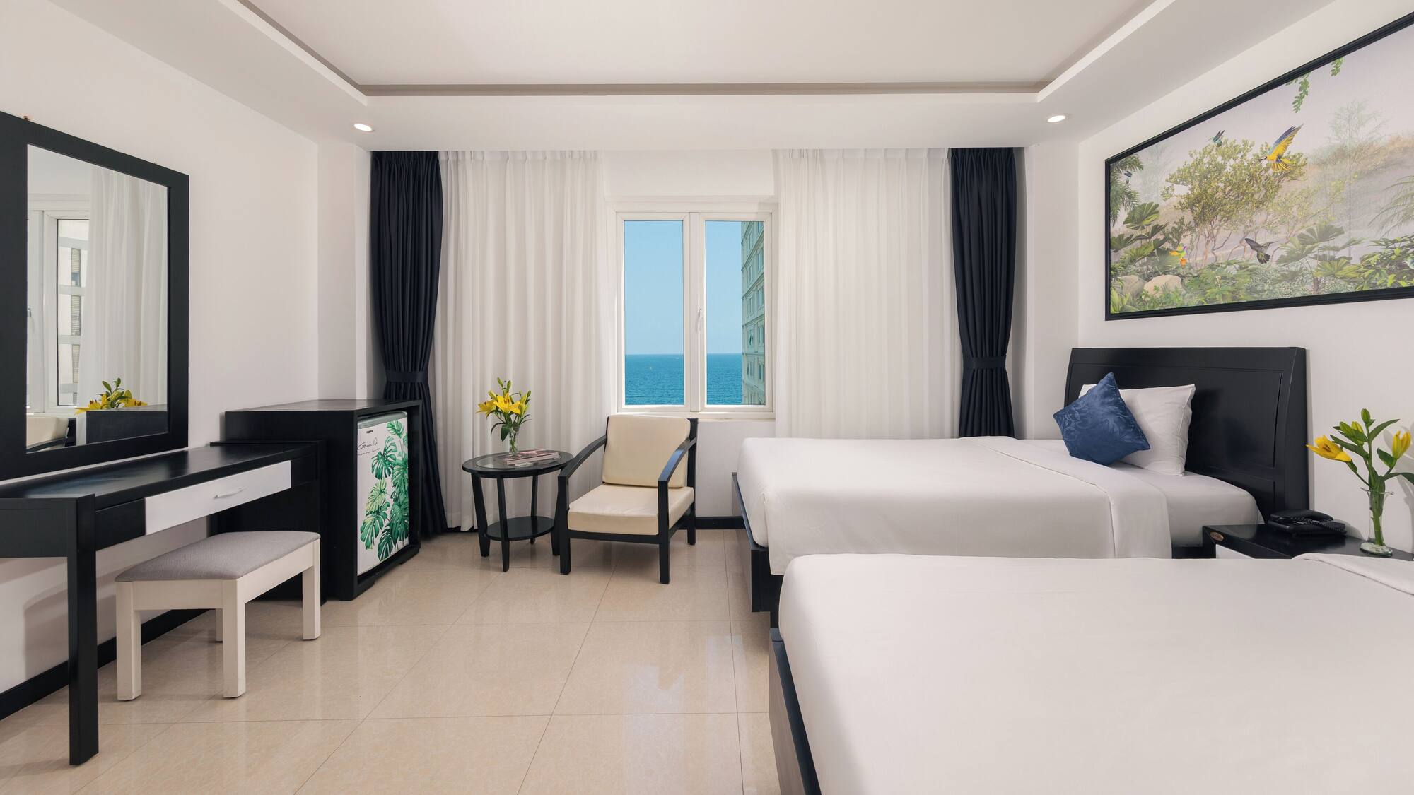 Phòng ngủ hai giường ga trắng, bàn trang điểm và cửa sổ giữa rèm xanh nhìn ra biển